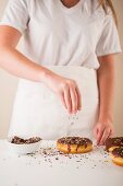 Doughnuts mit Schokoladenglasur mit bunten Zuckerstreuseln bestreuen