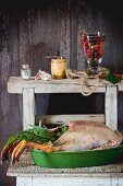 A ready-to-roast goose with a herb stuffing in a green roasting dish on a rustic wooden table