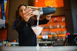 Junge Frau giesst fertigen Cocktail in ein Cocktailglas