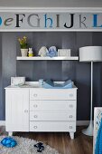 White baby-changing cabinet against grey-striped wallpaper and alphabet frieze in nursery