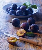 Fresh plums on a plate and on a wooden table, one halved