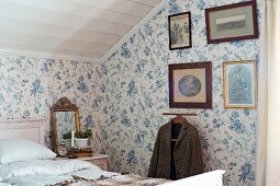 Schlafzimmer im Dachgeschoss mit floraler Tapete, alte gerahmte Fotos über stummem Diener