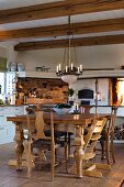 Rustic dining table, wooden chairs and candle chandelier in kitchen with wood-beamed ceiling