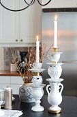 Gestapelte Vasen, Porzellandosen und Tassen als Kerzenleuchter