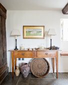 Table lamps on simple console table with drawers above vases and wicker basket on stone floor