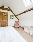 Double bed and dainty armchair in corner below exposed wooden roof beams