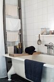 Candles on wooden board on free-standing bathtub next to old ladder used as towel rack