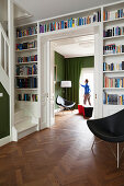 Foot of staircase in library with fitted bookcases, open sliding door and view of man standing between chairs