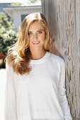 A blonde woman wearing a white top leaning against a wooden wall on a terrace