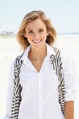 Junge Frau in weisser Bluse und gestreifter Strickweste am Strand