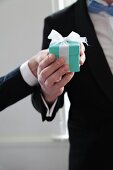 A man wearing a tuxedo holding a small gift