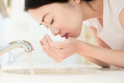 Asiatische Frau wäscht sich Gesicht am Waschbecken