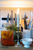 Brennende Kerze und Einmachglas mit eingelegten Birnen und Tannenzweig-Deko vor Küchenutensilien