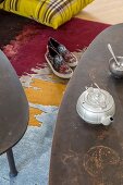 Vintage Teekanne auf Couchtisch, darunter Freizeitschuhe auf buntem Teppich