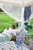 Garden pavilion furnished with bench, cushions and vintage fan on side table