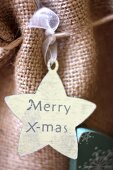 Star-shaped gift tag reading 'Merry X-mas' on hessian bag
