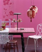 Mixture of styles in pink colour scheme: cake stand on dining table, various chairs and Oriental paper lanterns