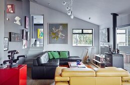 Black leather couch and yellow leather couch in open-plan, artistic interior with grey walls and gallery of pictures