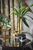 Vanity mirror, lily buds in gold vase and perfume bottles on round, mirrored bedside table