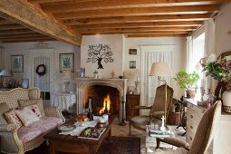 Comfortable living room with open fire, wood-beamed ceiling, curved couch and coffee table in old country house