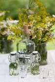 Bügelfläschchen mit Kräutern, grosse Flasche mit Korken und Blumenstrauss auf Gartentisch