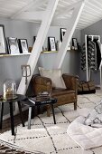 Leather armchair and side tables under pictures on narrow shelf and sloping ceiling