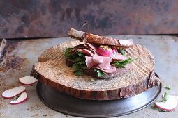 A pastrami and radish sandwich on a slice of wood