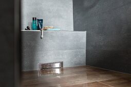 Detail of a floor-level, grey-tiled shower with bathing utensils on a narrow shelf