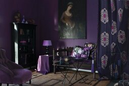 Room in shades of purple: armchair with mauve cover, antique bench below oil painting on aubergine wall and patterned curtain to one side