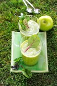 Two green smoothies garnished with lettuce and apple in the garden