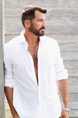 A dark haired man with a beard wearing a white shirt