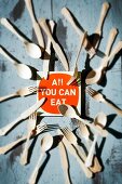 Schild mit Aufschrift: All you can eat, umgeben von Besteck