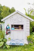 Giebelfassade eines Holz-Spielhauses in sommerlichem Garten und spielendem Mädchen