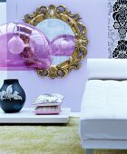 Round, gilt-framed mirror on lilac wall, white chaise and retro pendant lamp