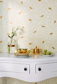 A white console table against a wall with golden bird silhouette wallpaper