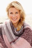 A blonde woman wearing a woollen shawl on a beach