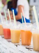 Various different types of apple juice on a market stand in plastic cups