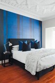 Elegant bedroom with black double bed and arranged scatter cushions, blue and black striped wallpaper and white stucco ceiling