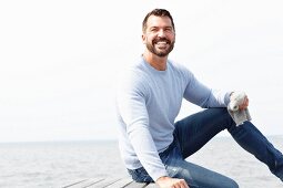 Mann mit hellblauem Pullover und Jeans am Meer