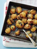 Hasselback potatoes with herbs on a baking tray (seen from above)