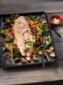 Salmon with broccoli, potatoes, carrots, root vegetables and mushrooms baked on a tray