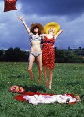 Two women in a meadow jumping into the air