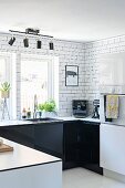 U-shaped kitchen counter with black cabinets against white-tiled wall and spotlights on rail mounted on ceiling