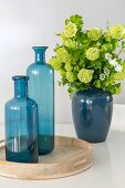 Two blue glass bottles on wooden tray and ceramic vase of lime-green hydrangeas