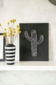 Fadenbild mit Kaktusmotiv und schwarz-weiss gestreifte Vase mit Trockenblumen