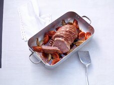 Meatloaf wrapped in bacon with tomatoes and onions in a roasting tin