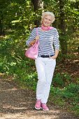 Blonde Frau in gestreiftem Shirt, weisser Hose und pinkfarbener Tasche in der Natur