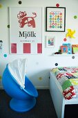 Child's blue pod chair and bed with colourful bedspread below posters on polka-dot wall