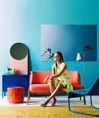 Young woman on orange sofa in front of turquoise wall