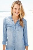 A young blonde woman on a beach wearing a denim shirt